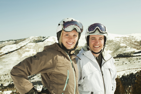Porträt eines glücklichen Paares in Skikleidung vor einem schneebedeckten Berg, lizenzfreies Stockfoto