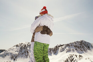 Skifahrer, die sich umarmen, während sie vor einem klaren Himmel stehen - CAVF01400