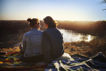 Rear view of couple sitting by lake during sunset - CAVF01418