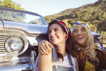 Happy women looking away while sitting against convertible car - CAVF01429