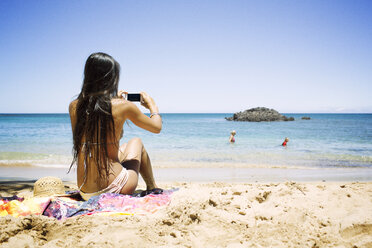 Rückansicht einer Frau beim Fotografieren am Strand - CAVF01458