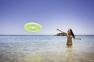 Woman throwing inflatable ring while standing in sea - CAVF01462