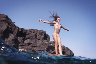 Smiling woman with arms outstretched jumping into water - CAVF01489