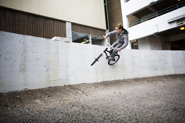 Cyclist performing stunt on retaining wall against building - CAVF01501