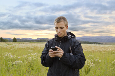 Mann, der ein Smartphone benutzt, während er auf einem Feld vor bewölktem Himmel steht - CAVF01510