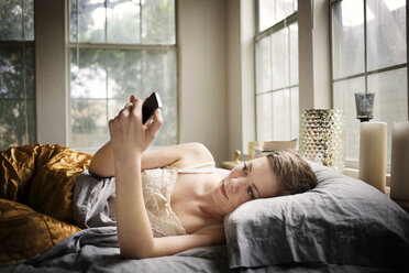 Woman using smart phone while lying on bed at home - CAVF01517