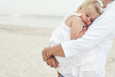 Mittelteil einer Mutter, die ein Mädchen trägt, während sie am Strand steht - CAVF01522