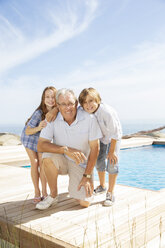 Grandfather and grandchildren smiling at poolside - CAIF07940