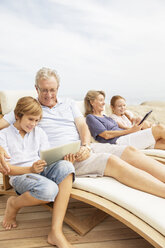 Großeltern und Enkelkinder nutzen digitale Tablets am Swimmingpool - CAIF07943