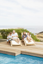 Älteres Paar und Enkelkinder entspannen am Pool - CAIF07955
