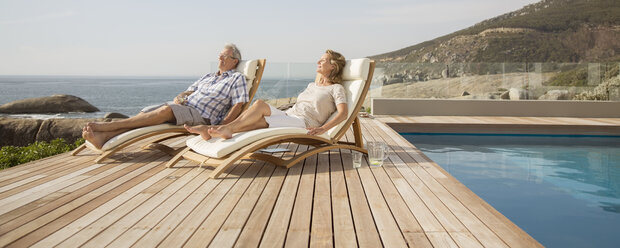 Älteres Paar entspannt sich in Liegestühlen am Pool - CAIF07964