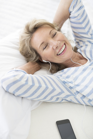 Ältere Frau mit Kopfhörern auf dem Bett, lizenzfreies Stockfoto
