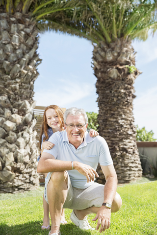Älterer Mann und Enkelin lächelnd im Hinterhof, lizenzfreies Stockfoto