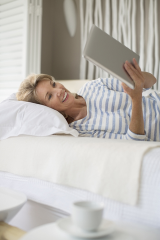 Ältere Frau benutzt digitales Tablet auf dem Bett, lizenzfreies Stockfoto