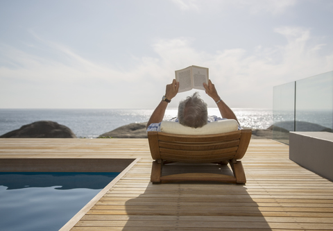 Older man reading by pool stock photo