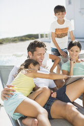 Familie benutzt digitales Tablet auf Liegestühlen am Pool - CAIF08047