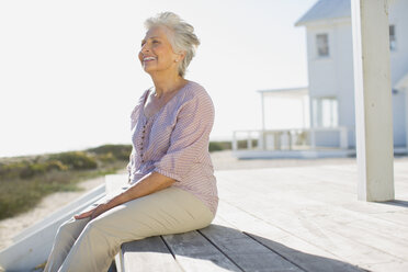 Ältere Frau sitzt auf der Terrasse vor einem Strandhaus - CAIF08051