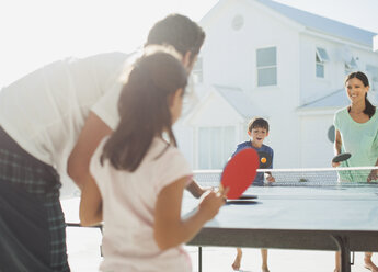 Family playing table tennis outside house - CAIF08059