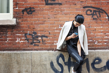 Frau benutzt Smartphone und lehnt sich an eine Mauer - CAVF01595