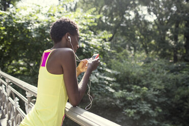 Woman using mobile phone while leaning by railing at park - CAVF01601