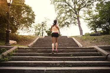 Rear view of woman exercising on steps in park - CAVF01612