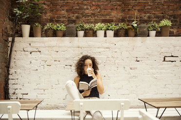 Frau liest ein Buch und trinkt Kaffee in einem Straßencafé - CAVF01624