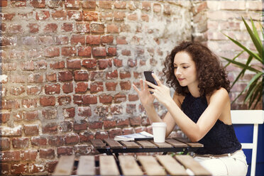 Frau, die ein Mobiltelefon benutzt, während sie in einem Straßencafé sitzt - CAVF01627