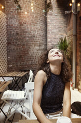 Smiling woman looking up while sitting in sidewalk cafe - CAVF01628