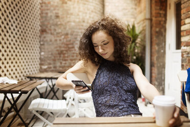 Woman using phone while sitting in sidewalk cafe - CAVF01629