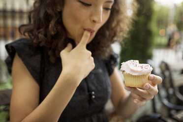 Frau isst Muffin, während sie in einem Straßencafé sitzt - CAVF01634
