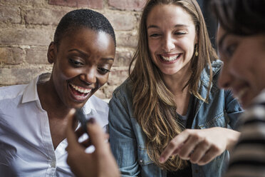 Frau zeigt Freunden ihr Smartphone, während sie in einem Cafe sitzt - CAVF01698