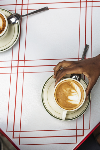 Ausgeschnittenes Bild einer Hand, die einen Cappuccino in einem Straßencafé hält, lizenzfreies Stockfoto