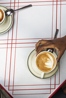 Ausgeschnittenes Bild einer Hand, die einen Cappuccino in einem Straßencafé hält - CAVF01709