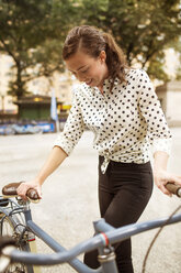 Woman holding bicycle while standing on road in central park - CAVF01717