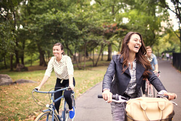 Happy friends cycling on road in central park - CAVF01724