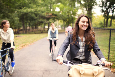 Female friends cycling on road in central park - CAVF01725