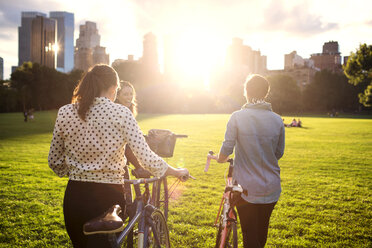 Rückansicht von Frauen, die mit Fahrrädern auf einem Feld im Central Park spazieren gehen - CAVF01732