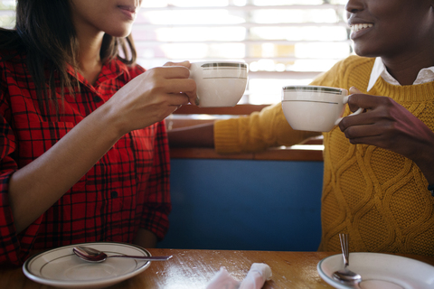 Midsections von Freunden trinken Cappuccino während sie in einem Café sitzen, lizenzfreies Stockfoto