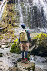 Rückansicht eines Wanderers mit Rucksack, der vor einem Wasserfall steht - CAVF01787