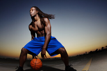 Man looking away while playing with basketball on road against clear sky - CAVF01913