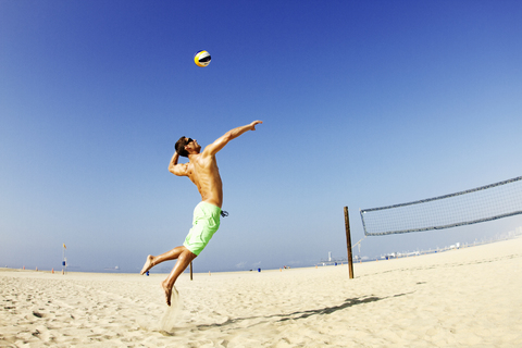 Mann schlägt Ball am Strand gegen klaren Himmel, lizenzfreies Stockfoto