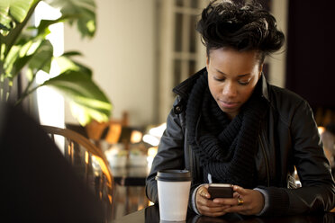 Frau, die ein Mobiltelefon benutzt, während sie in einem Cafe sitzt - CAVF01979