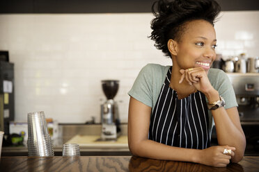 Happy woman looking away while standing at counter in cafe - CAVF01987