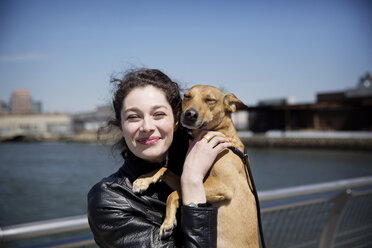 Portrait of happy woman with dog standing on footbridge against sky - CAVF02010