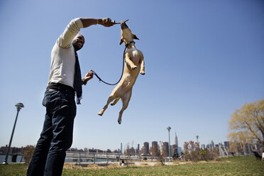 Niedriger Blickwinkel auf einen Mann, der mit einem Hund spielt, während er auf einem Feld vor einem klaren Himmel steht - CAVF02012