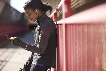 Woman listening music while leaning on fence at Williamsburg Bridge pedestrian walkway - CAVF02020