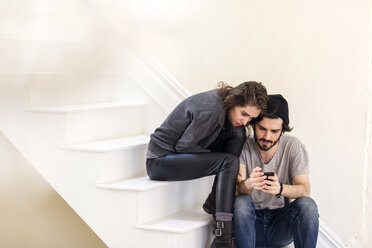 Couple looking at smart phone while sitting on staircase - CAVF02061