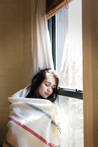 Frau mit geschlossenen Augen, die sich zu Hause ans Fenster lehnt, lizenzfreies Stockfoto