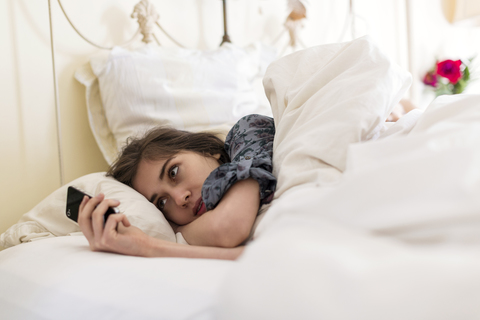 Woman using mobile phone while lying on bed stock photo