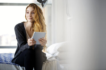 Woman with tablet computer looking away while sitting on bed at home - CAVF02093